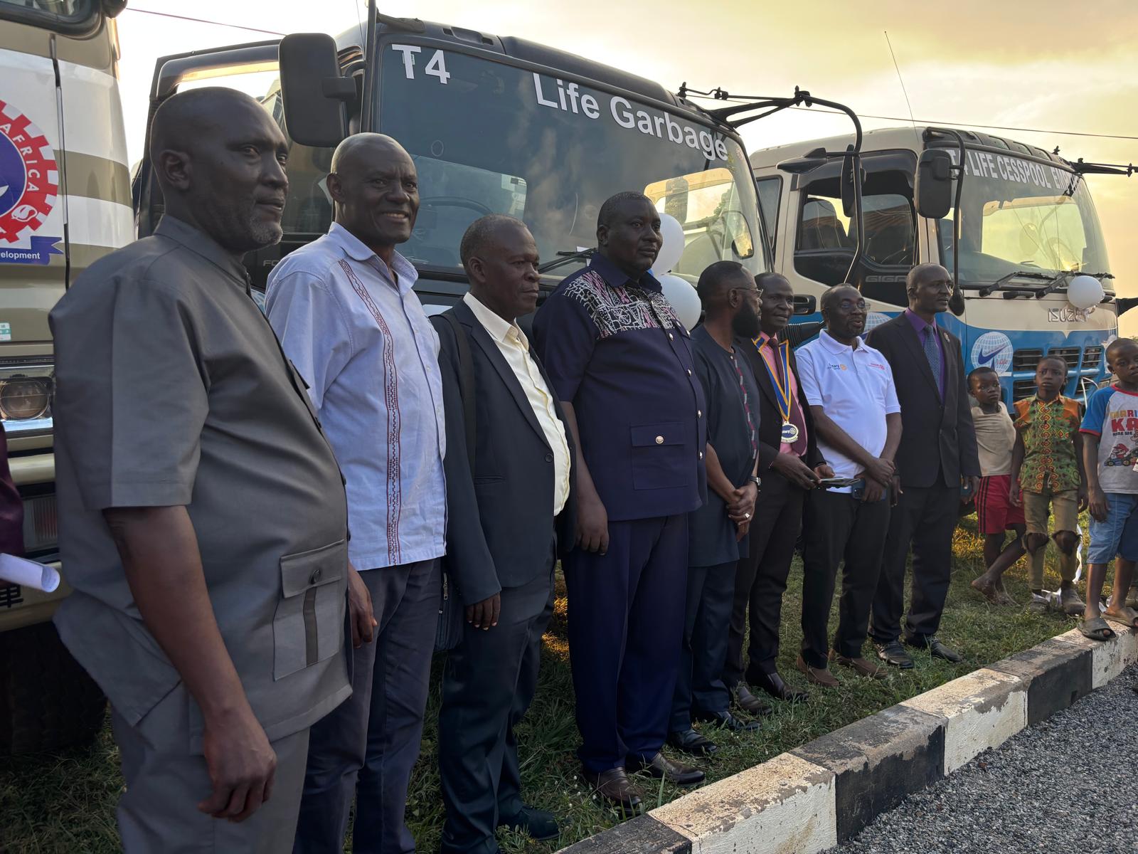 A line of officials in front of the T4 Life garbage truck and cesspool emptier, with children watching