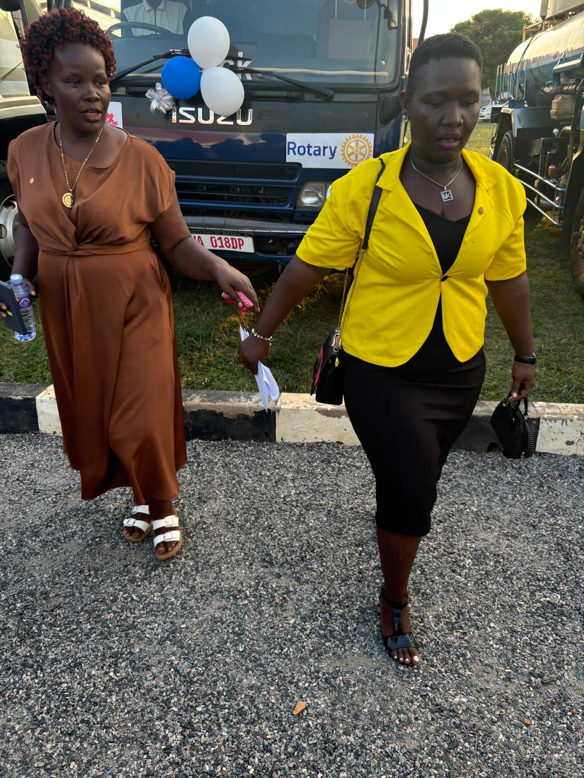 Two women carrying the ceremonial ribbon and scissors past the ISUZU garbage truck