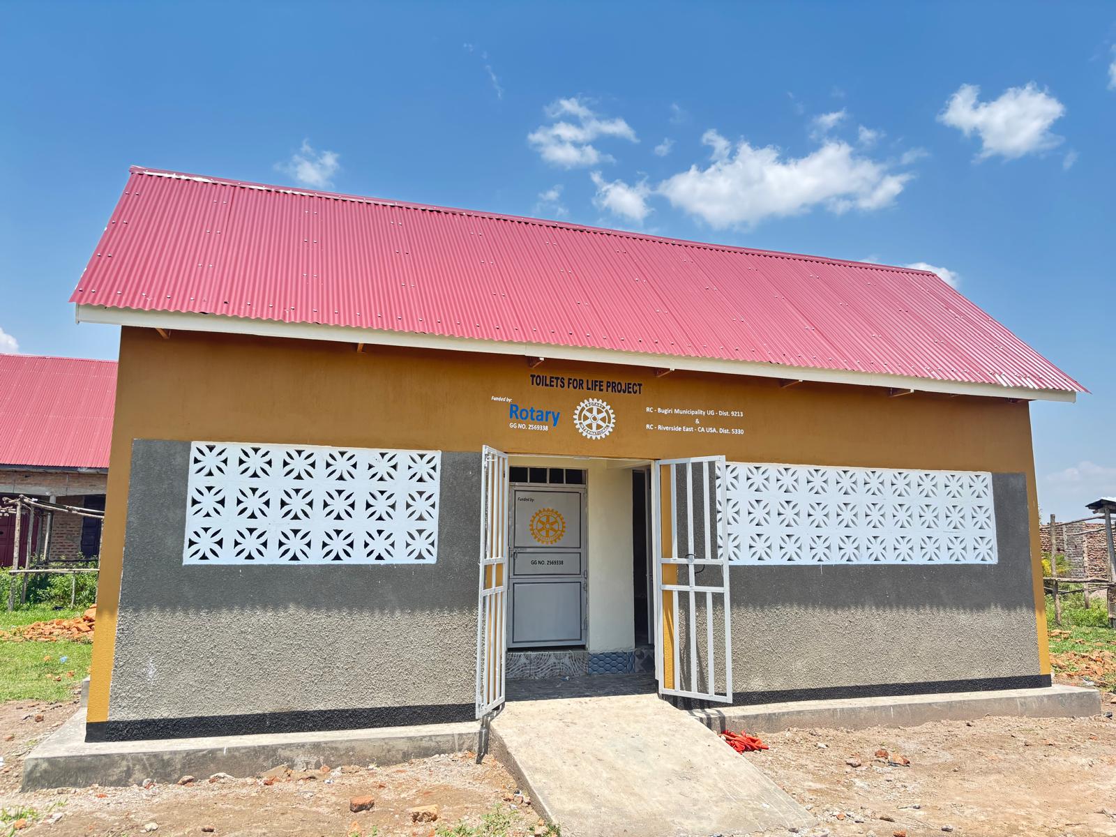 Front view of a completed Toilets 4 Life Phase II sanitation block with a red roof and painted Rotary signage